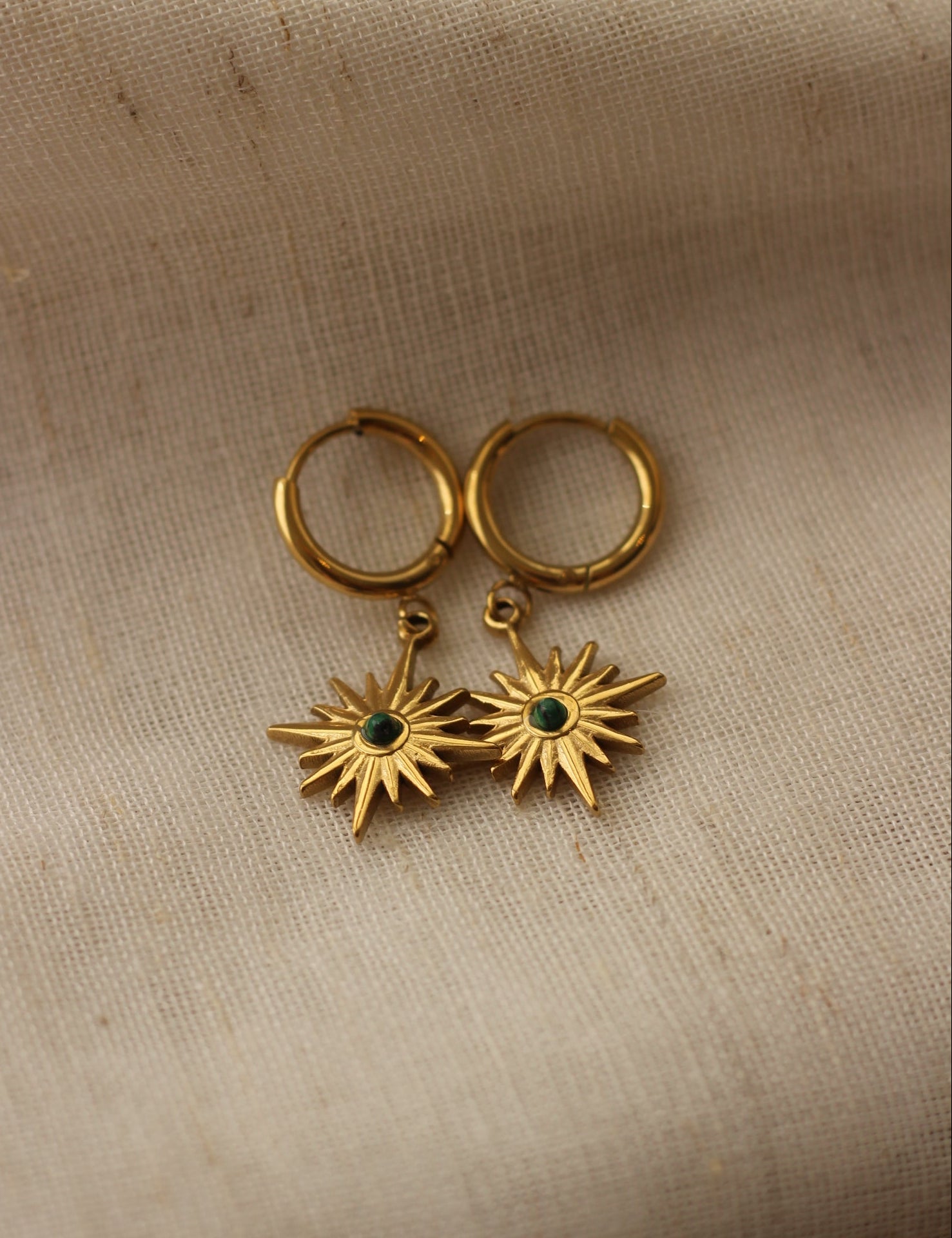 Gold earrings with star designs on a beige fabric background
