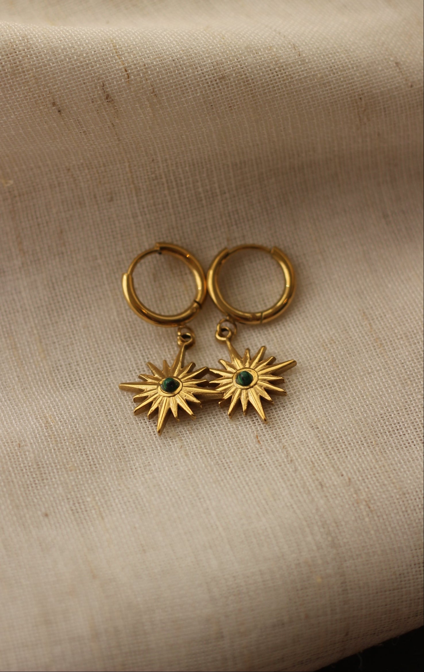 Gold earrings with star designs on a beige fabric background