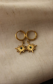 Gold earrings with star designs on a beige fabric background